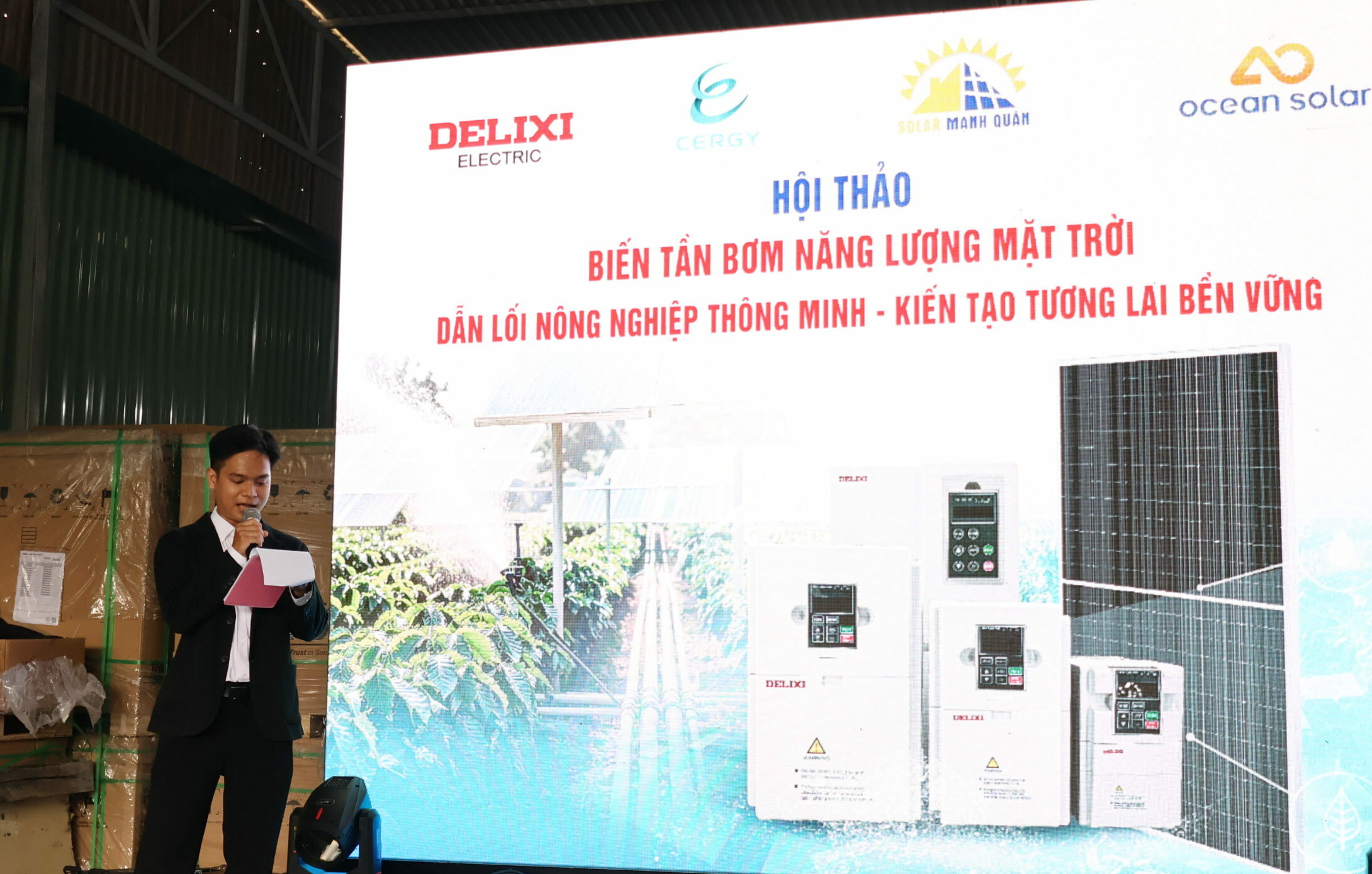 Người phát biểu đang thuyết trình tại hội thảo với backdrop lớn hiển thị thông tin về biến tần bơm năng lượng mặt trời, với logo của Delixi Electric, Cergy, Mạnh Quân Solar và Ocean Solar.